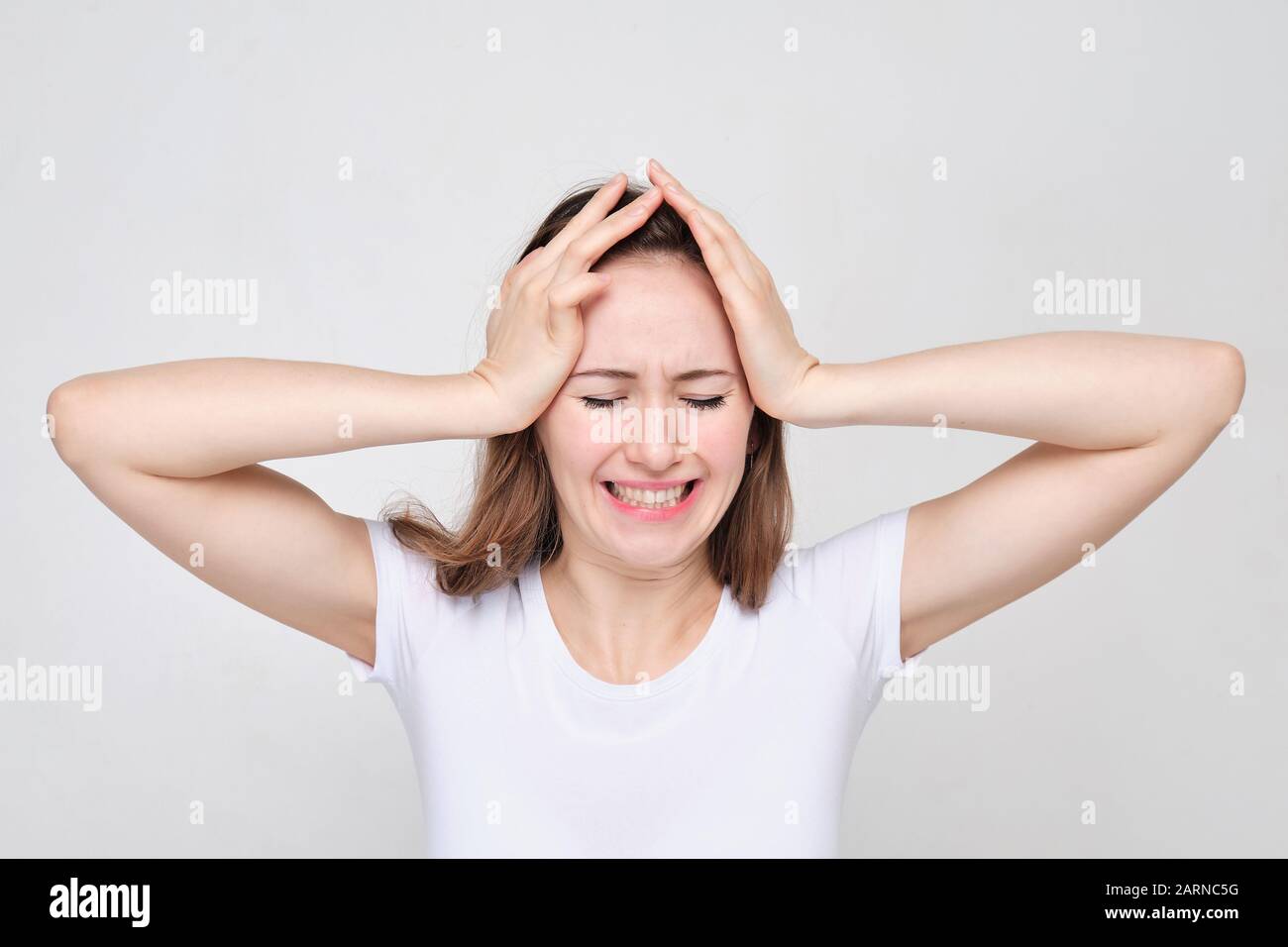 A girl in a white T-shirt holds head with her hands. The concept of stress and problems. Close up. Stock Photo