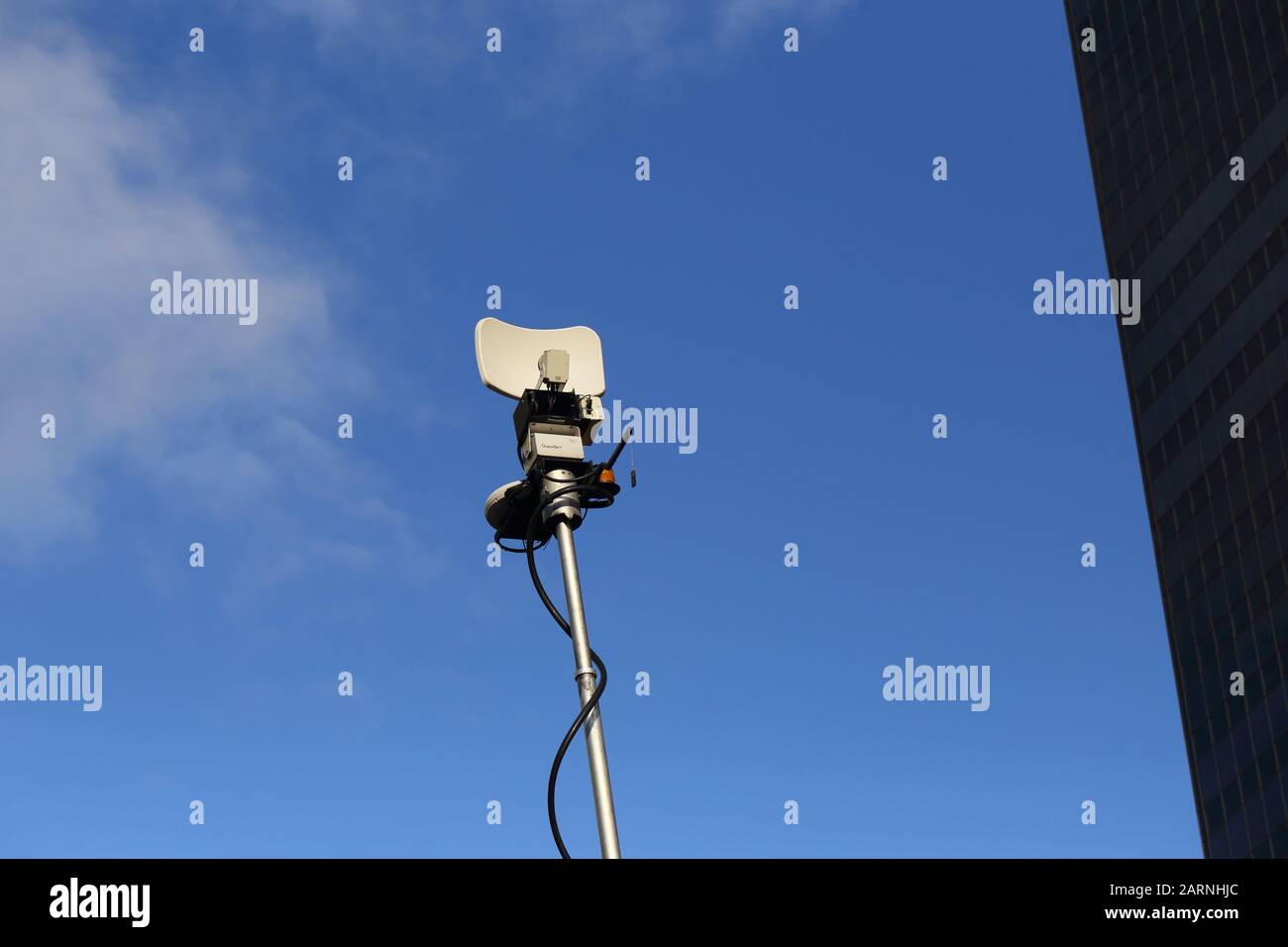 A tv van satellite dish in a blue sky with a sliver of building Stock