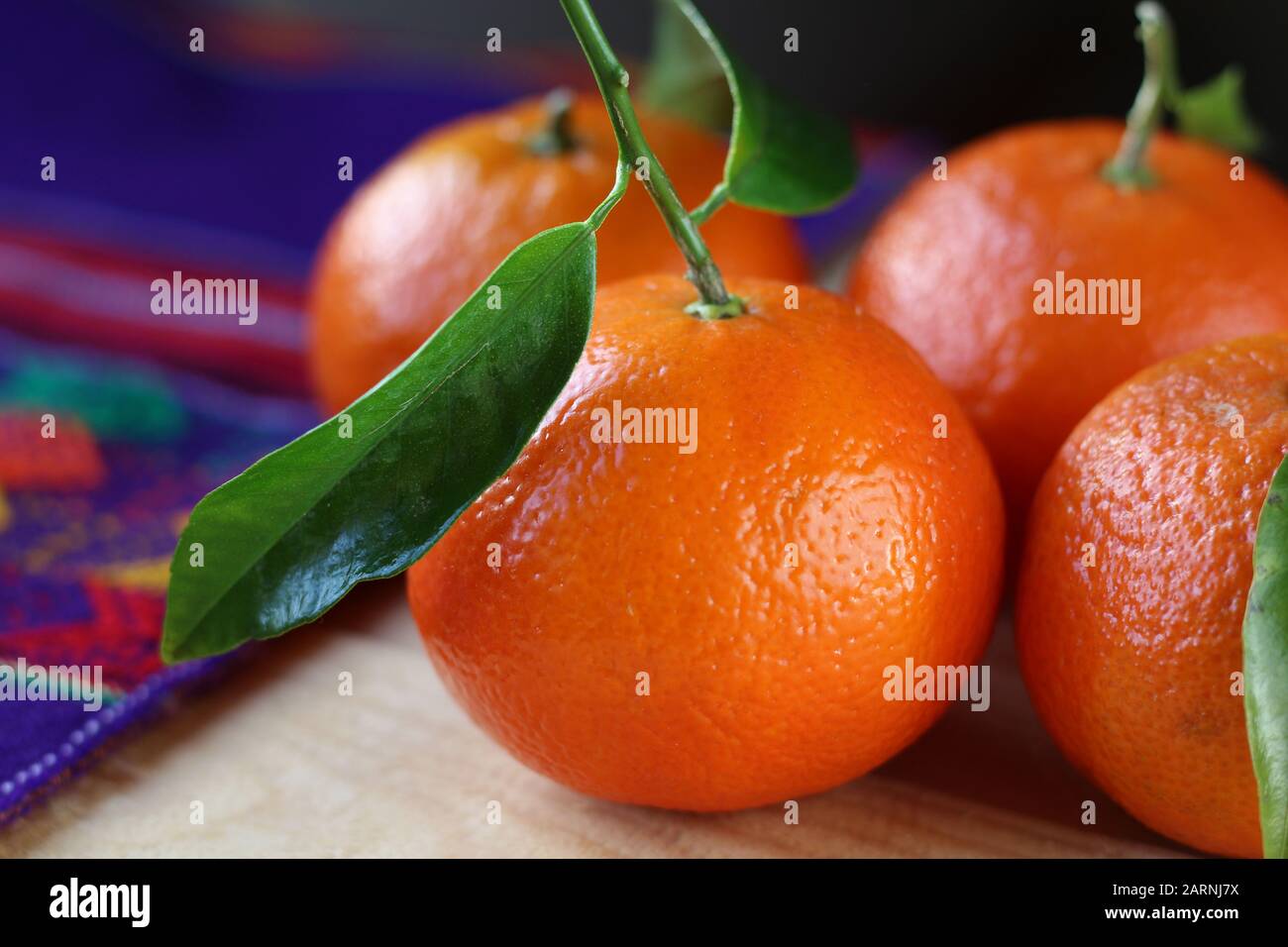 Side on view of fresh ripe mandarin oranges in close up, on a wooden table with colorful purple table cloth, with copyspace. Citrus reticulata Stock Photo