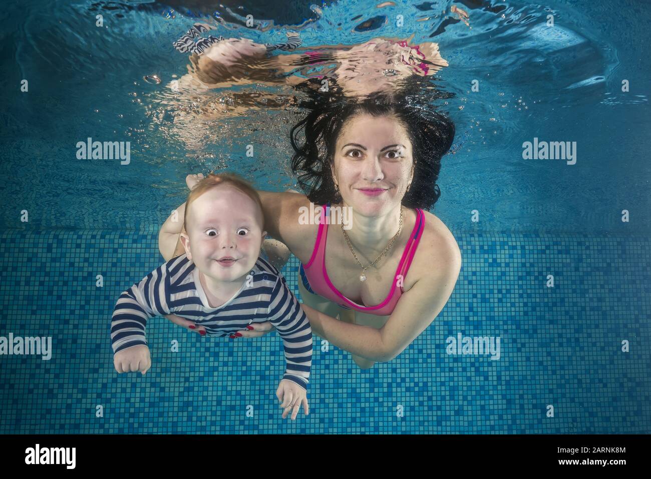 Little baby boy learning to swim underwater in a swimming pool, mother