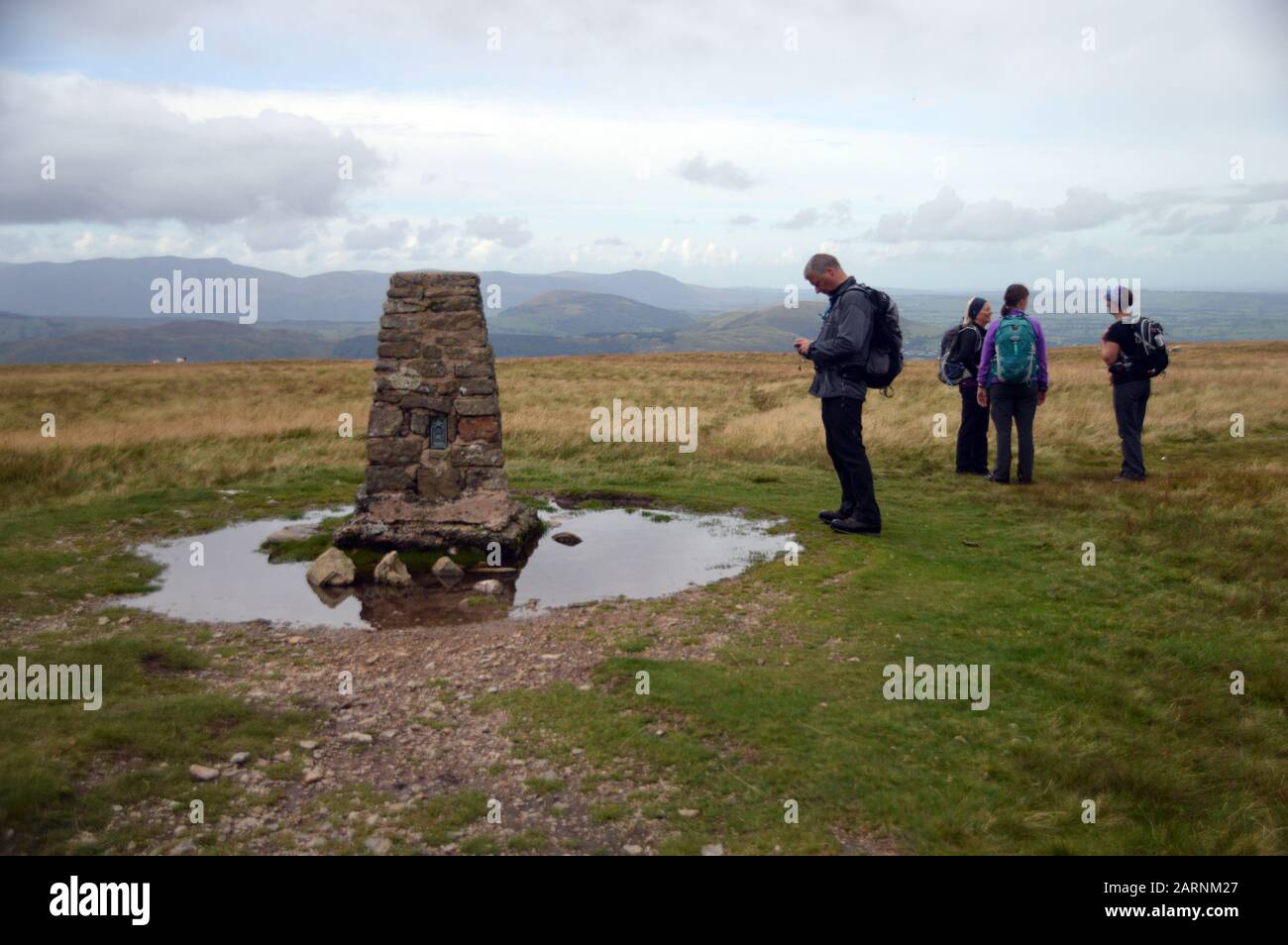 Man Checking GPS Compass & Women Talking by the Summit Cairn of the Wainwright 'Loadpot Hill' in the Lake District National Park, Cumbria, England. Stock Photo