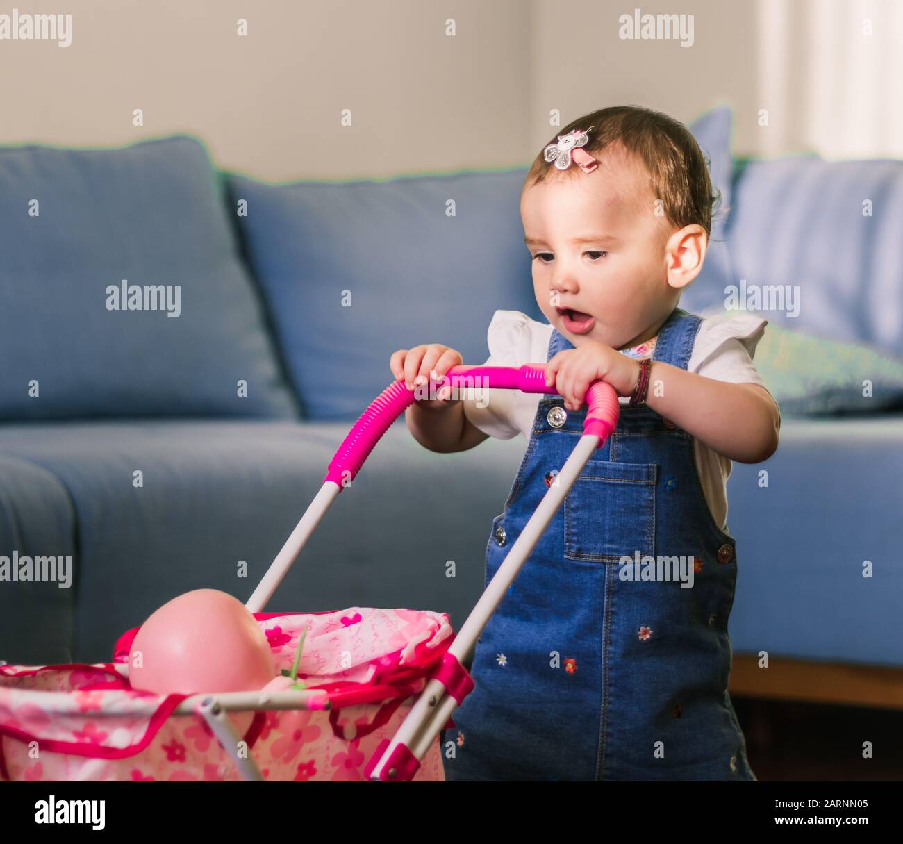 portrait of a cute little baby girl playing mothers and daughters with her pink doll in the buggy. Stock Photo