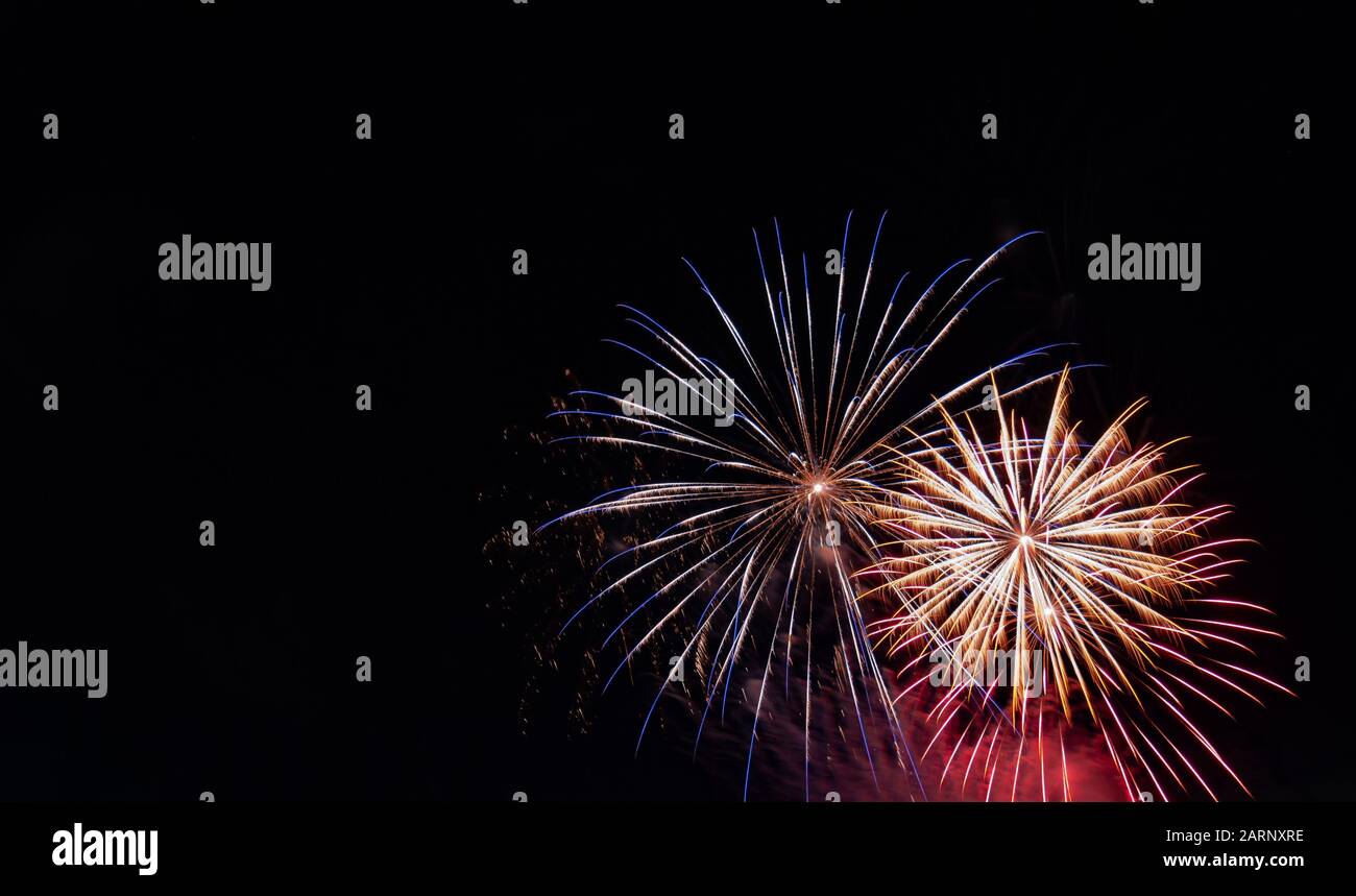 Blue-tipped white starburst firework beside a white starburst firework with red highlights photographed against a black sky on the Fourth of July Stock Photo