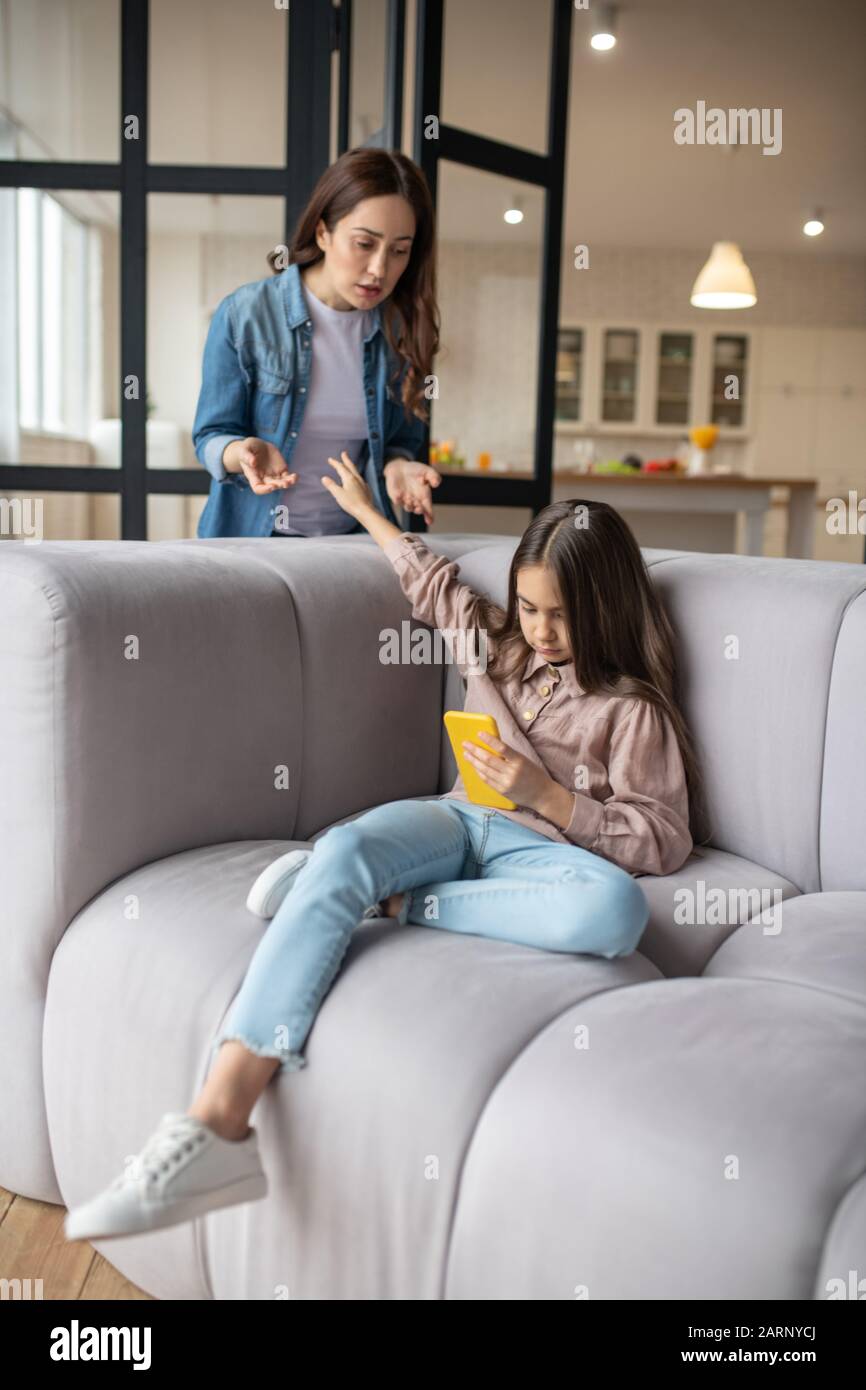 Naughty daughter with smartphone in her hand sitting on couch. Stock Photo