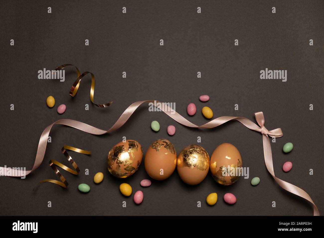 Happy easter concept. Golden eggs, color candy on a dark background, Layout or template for banner, article, product advertisement. Stock Photo
