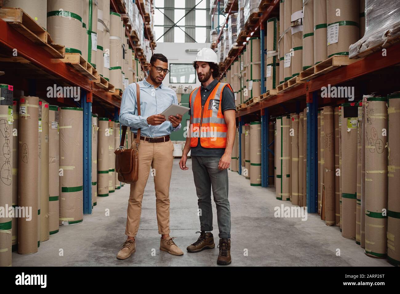 Young banker in conversation with warehouse manager holding digital tablet discussing loan details for sanction Stock Photo