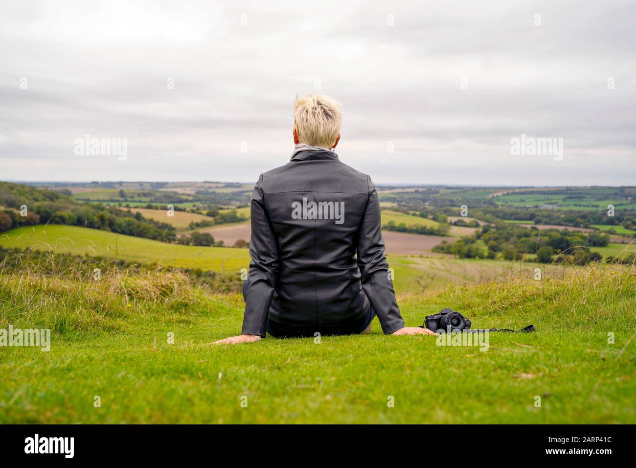 Blond woman with camera aside contemplating hilly green landscape Stock Photo