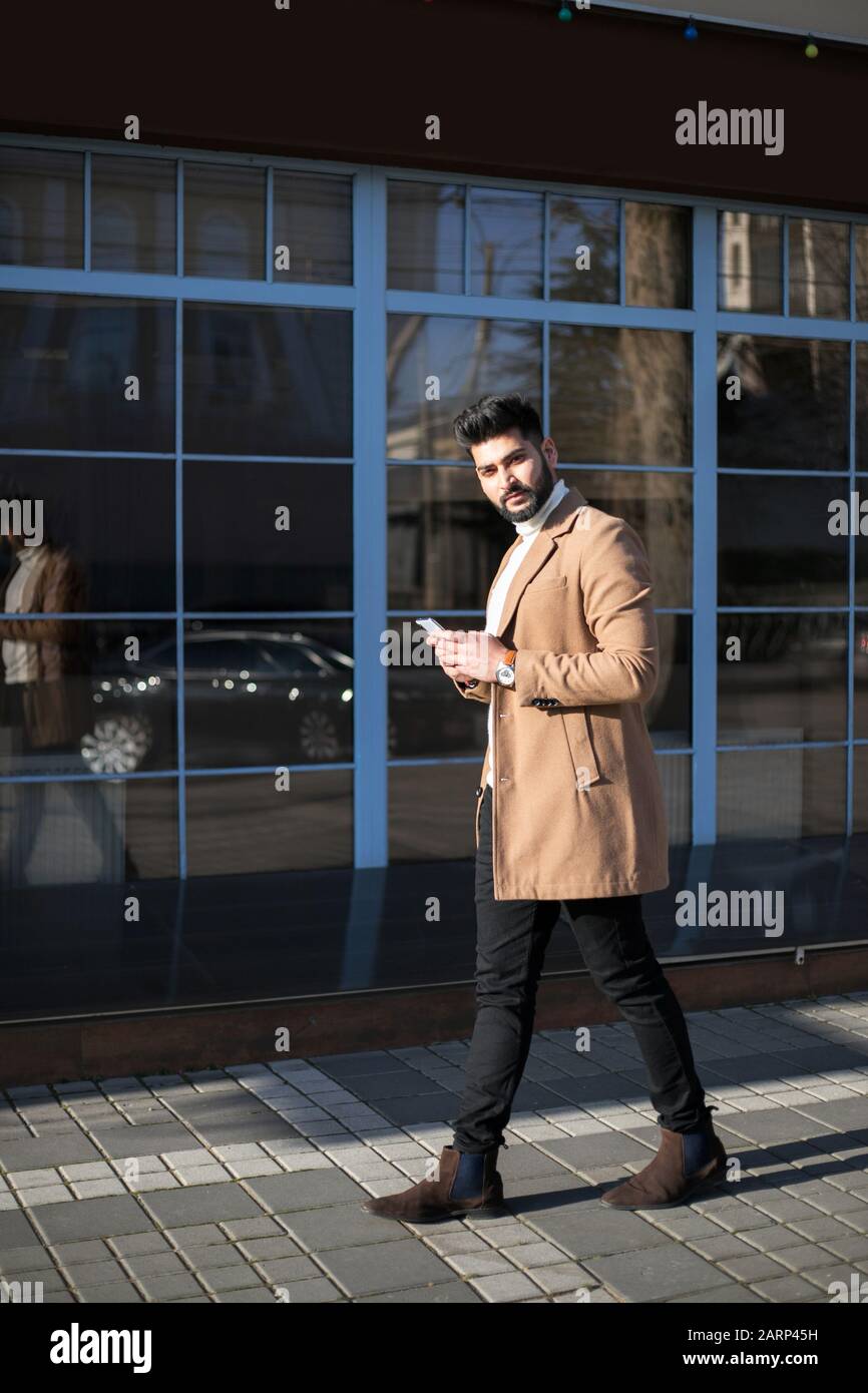 Young Indian businessman using his smartphone at street while walking. Stock Photo