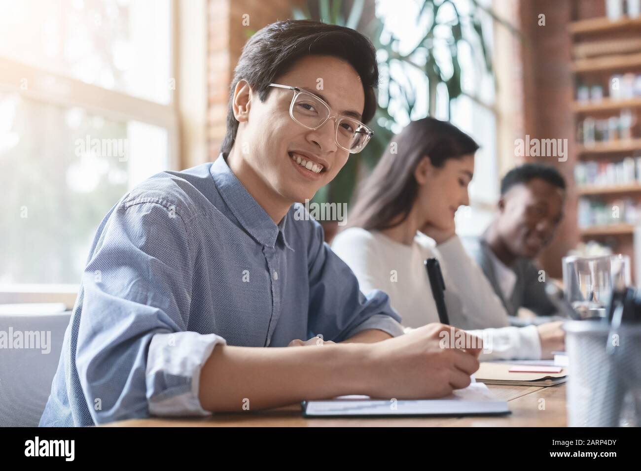 Smiling asian guy taking notes while business meeting with colleagues Stock Photo