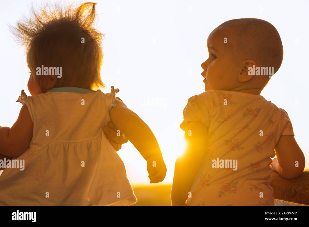 two cute baby girls contemplating sunset on the balcony. Stock Photo