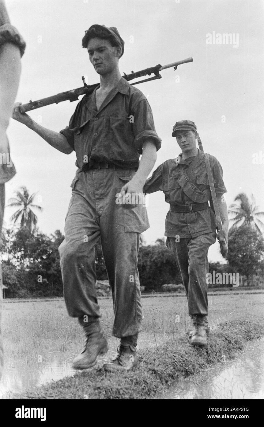 Two Dutch soldiers walk across a dike in a rice field. The front has a ...