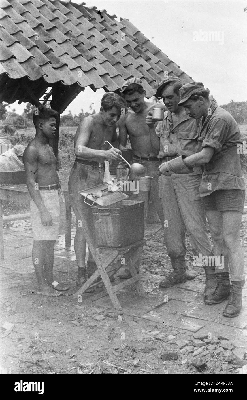 Four soldiers around a gamel with soup? On the left is an Indonesian man (cook?). Right man with gloves and leather belt Date: 1947/01/01 Location: Indonesia, Dutch East Indies Stock Photo