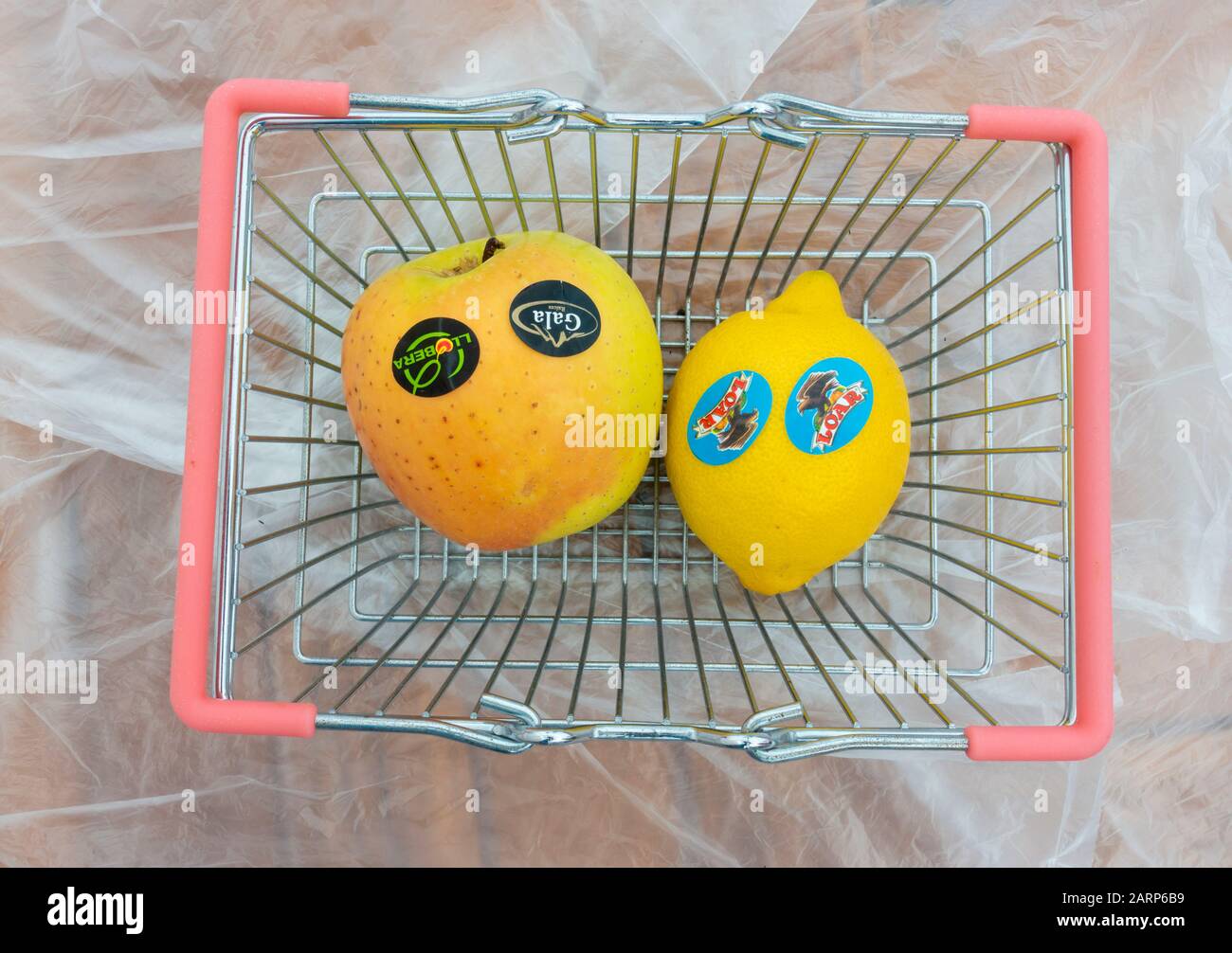 Plastic stickers on supermarket fruit in small basket on thin plastic bags background. Stock Photo