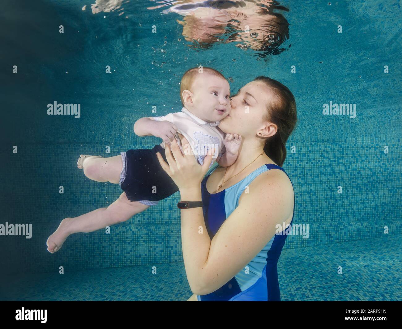 In blue pool young mother swimming with happy baby son dives