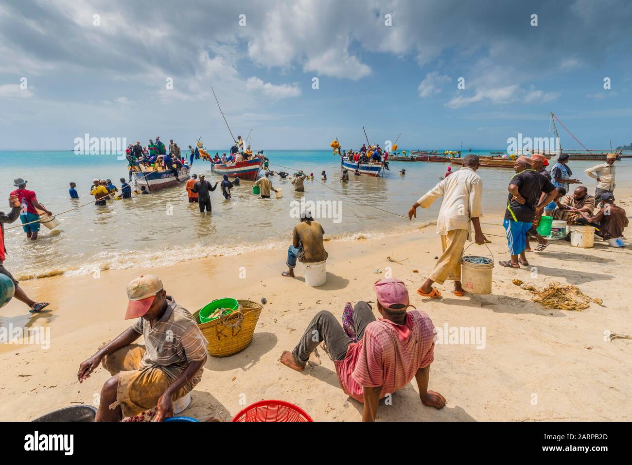 Zanzibar. Fishing boats anchor off the beach and vendors wade out to shoulder depth, buy fish, return to the beach and set up tables to start selling . Stock Photo