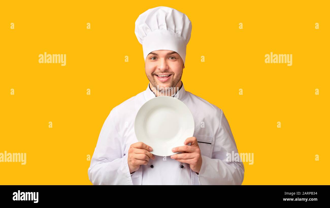 Chef Guy Posing Holding Empty Plate, Yellow Studio Background, Panorama Stock Photo