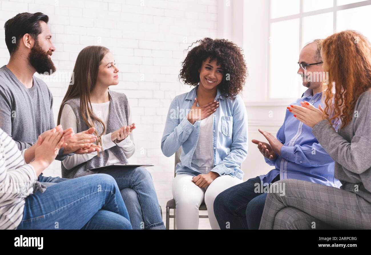 Happy afro woman appreciating support of people at rehab group meeting Stock Photo