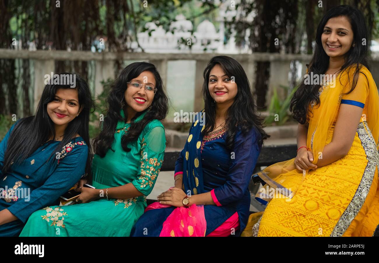 Group of four beautiful, smiling women in traditional clothes sitting on bench in Udaipur, Rajasthan, India. Stock Photo