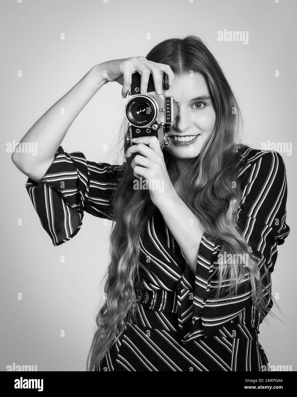 Young woman posing in retro 70's outfit with a film camera in studio setting Stock Photo