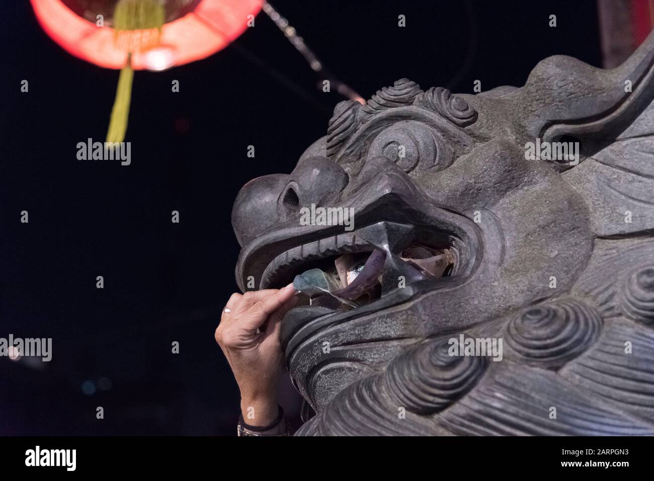 Capital Federal, Buenos Aires / Argentina; Jan 25, 2020: hand introducing money into the mouth of a chinese guardian lion statue, in the celebrations Stock Photo