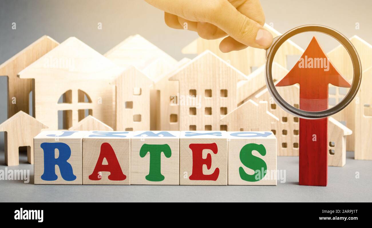 Wooden blocks with the word rates, up arrow and miniature houses. The concept of high interest rates on mortgages. Real estate. Credit. Loan Stock Photo