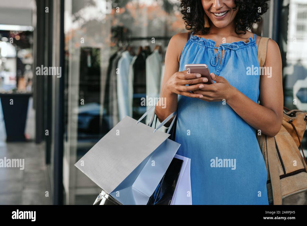 Smiling woman using her cellphone while out shopping for clothes Stock Photo