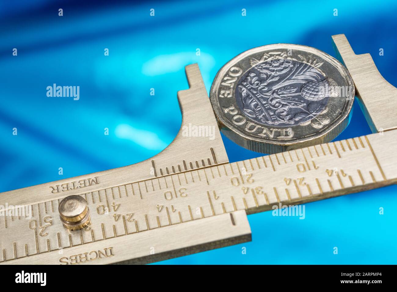 UK new pound coin between brass Vernier caliper jaws. For price