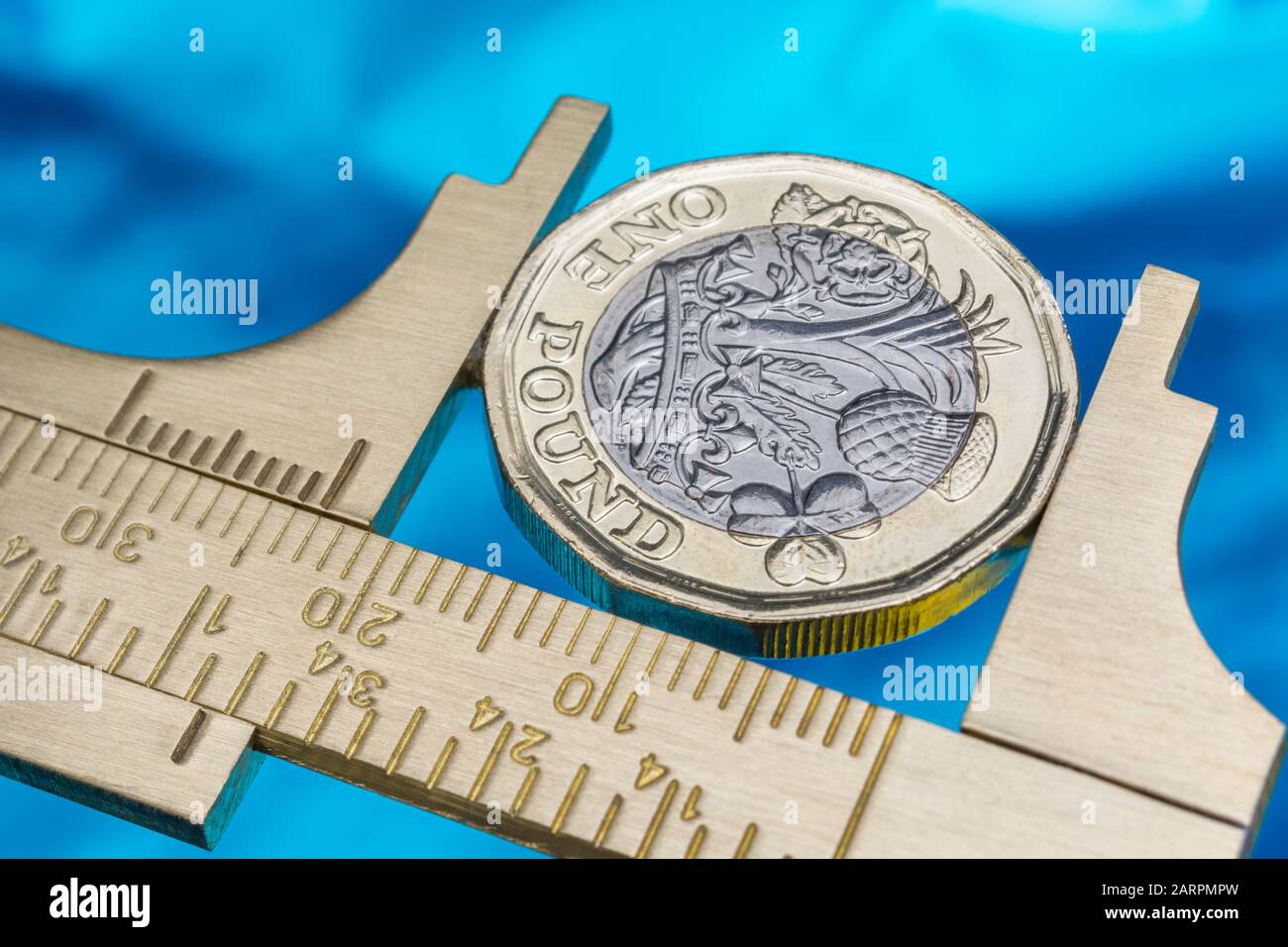 UK new pound coin between brass Vernier caliper jaws. For price