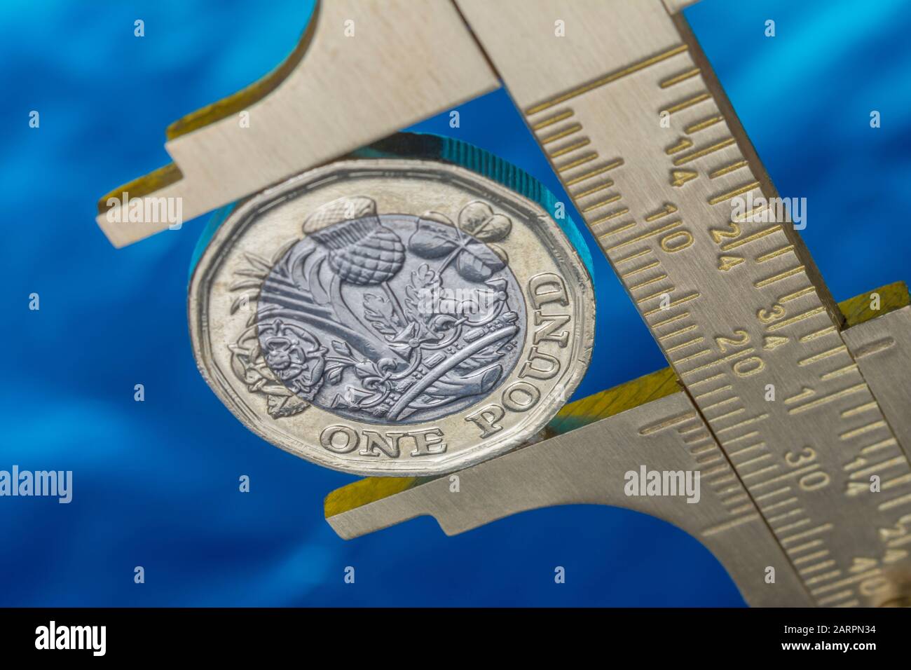 UK new pound coin between brass Vernier caliper jaws. For price