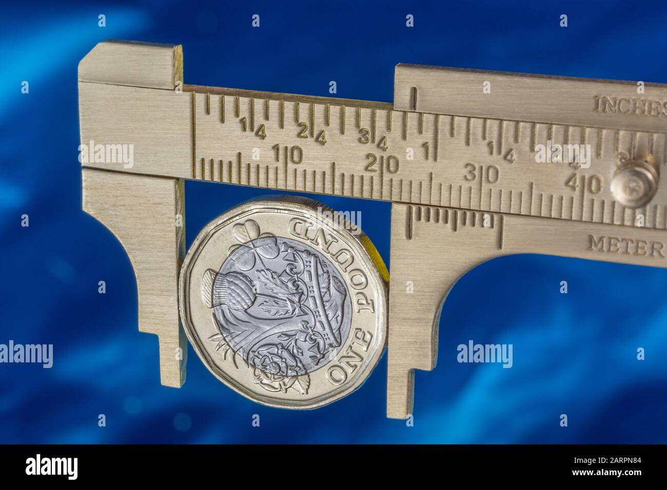 UK new pound coin between brass Vernier caliper jaws. For price