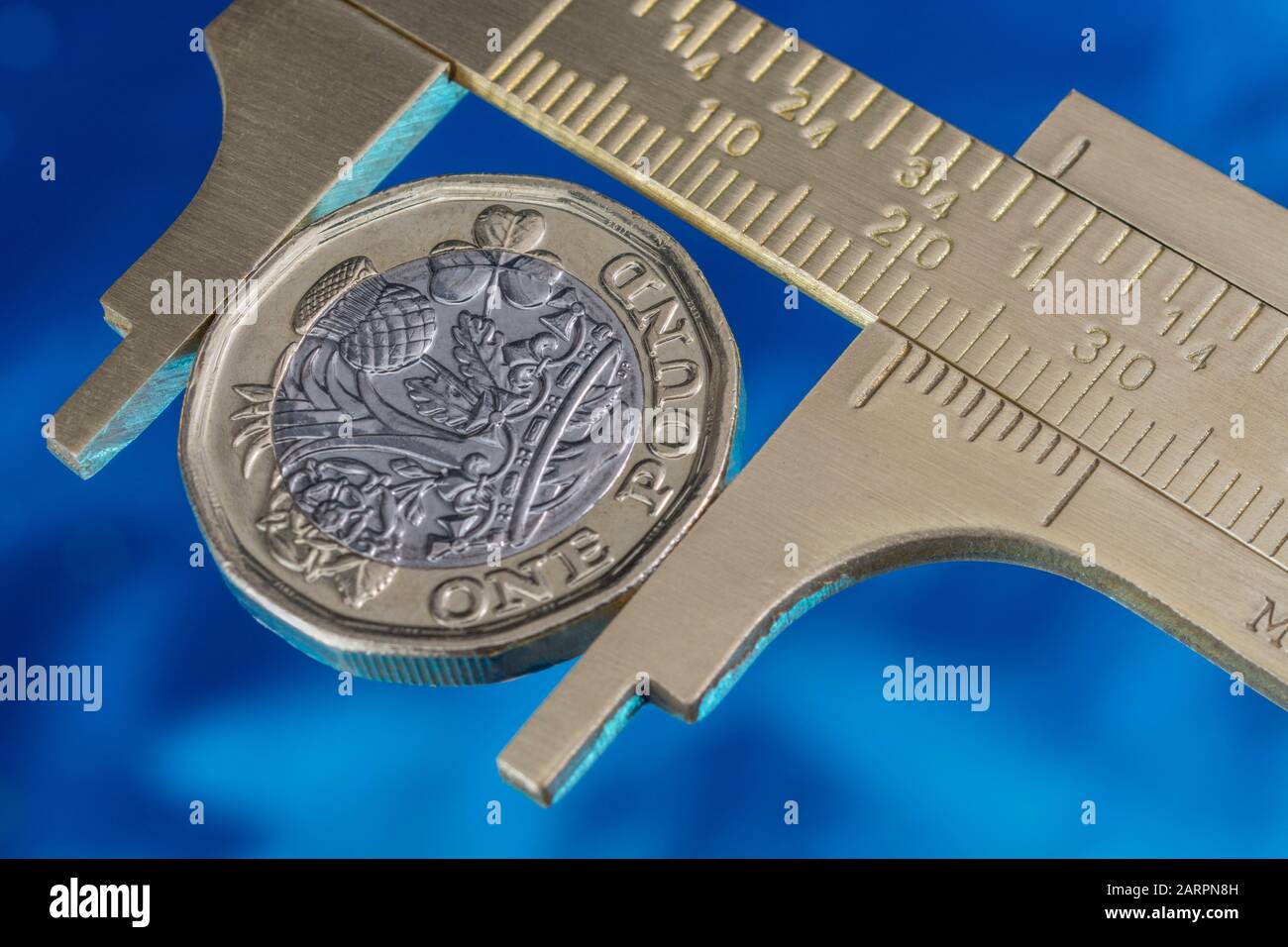 UK new pound coin between brass Vernier caliper jaws. For price