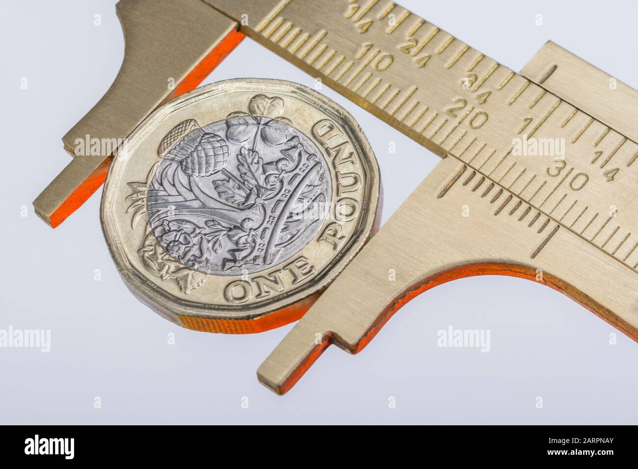 UK new pound coin between brass Vernier caliper jaws. For price
