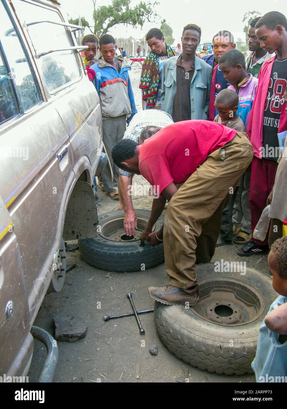 Local Ethiopians look with curiosity at the repair of the rear wheel in a jeep. Ethiopia. Stock Photo