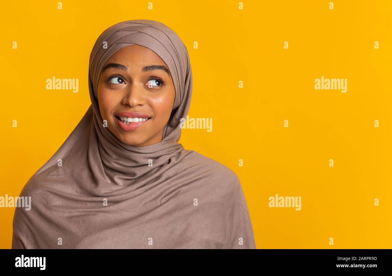 Doubtful black muslim woman in headscarf biting lip and looking aside Stock Photo