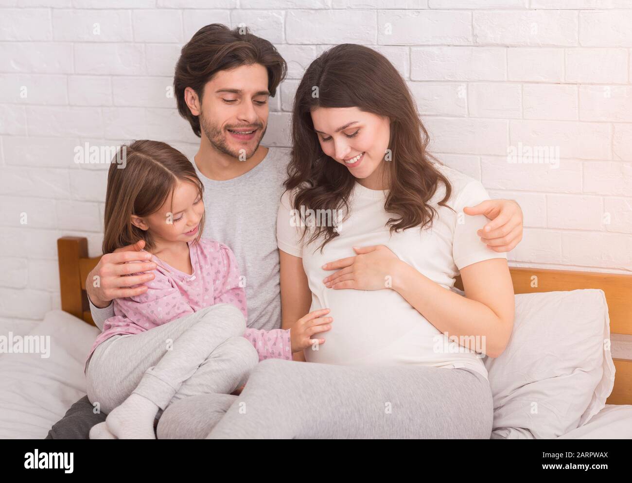 Pregnant woman, her husband and daughter cuddling together on bed Stock