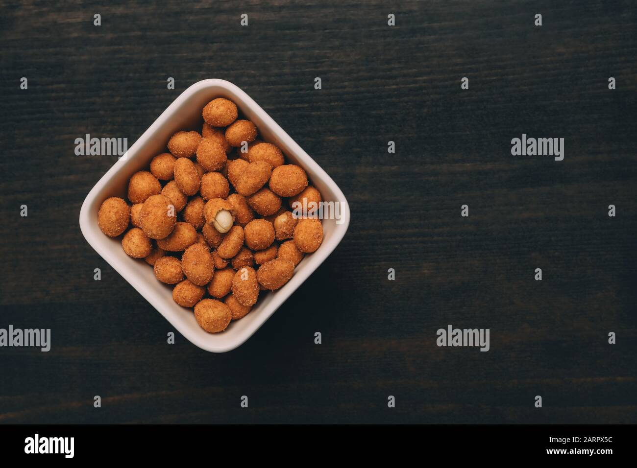 Salty peanut snack coated with barbecue sauce served in ceramic bowl on table, top view Stock Photo