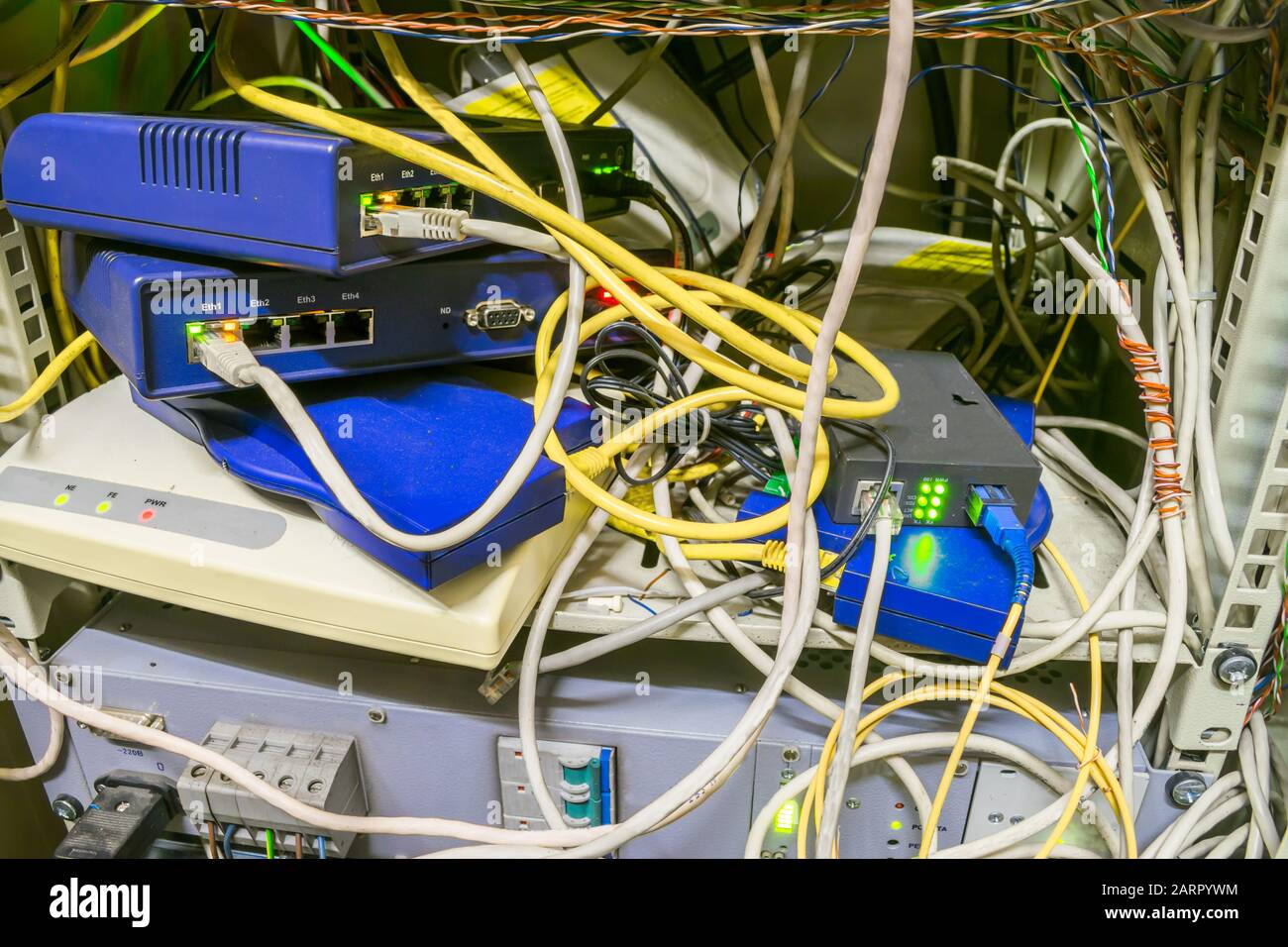 Chaotic interlacing of wires between modems, switches and Internet bridges. Rack with many network devices and cables. Box with network communication Stock Photo