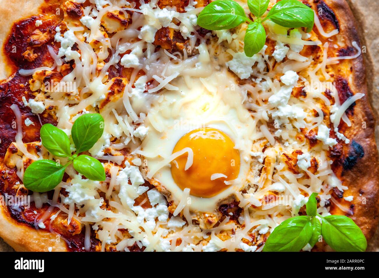 Close up shot of a pizza with egg, cheese and herbs. Rustic scene and dramatic light. Stock Photo