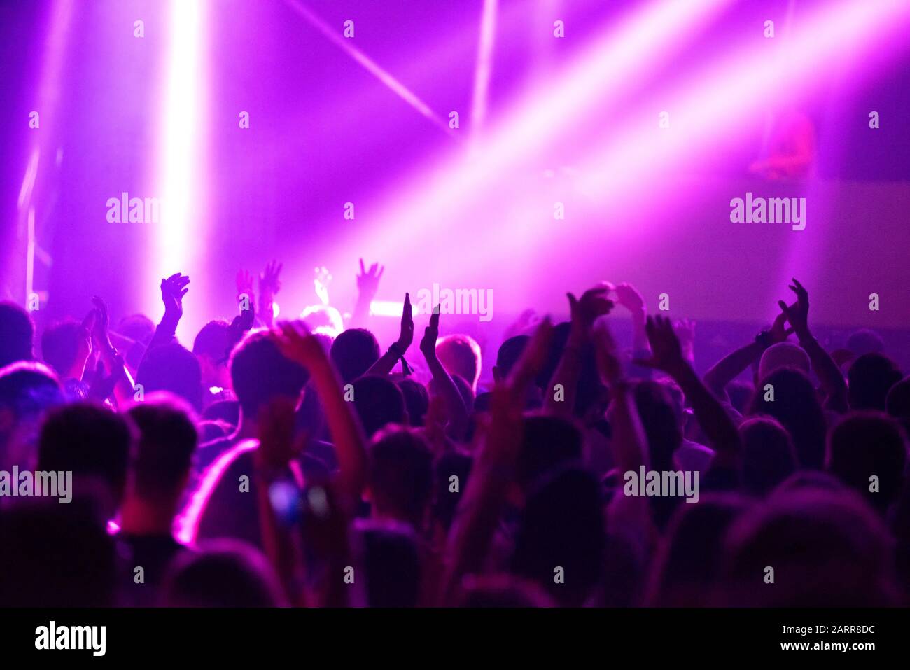 Blurred image of silhouette of raised arms, crowd of people in the front of bright stage lights at popular music concert Stock Photo