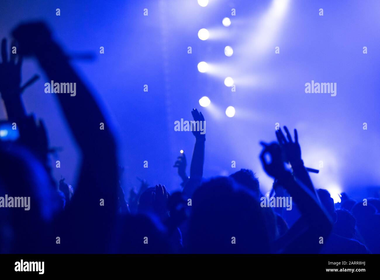 Silhouette of raised arms, crowd of people in the front of bright stage lights at popular music concert Stock Photo