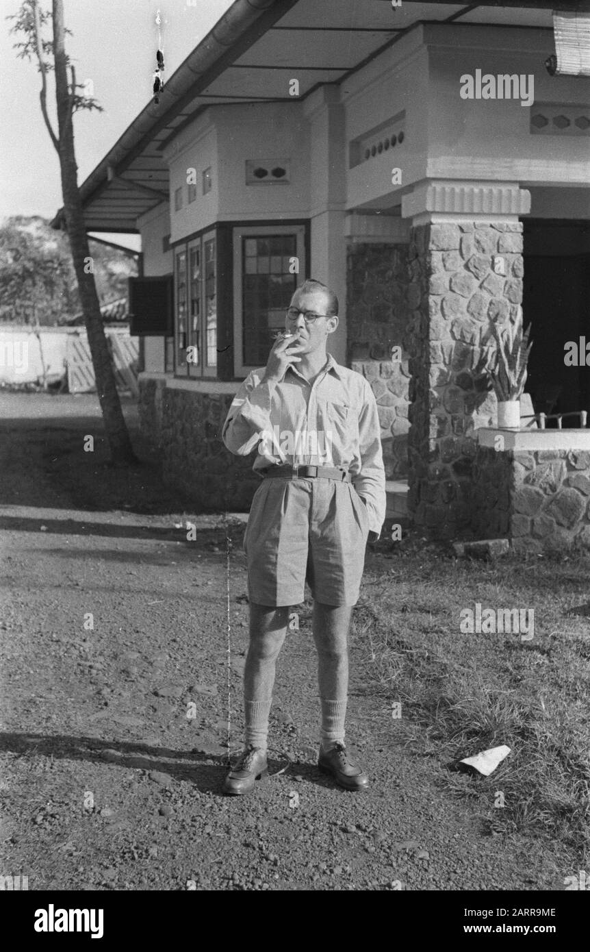 Pass photos X  [Smoking man with glasses and shorts, standing in front of a gate building] Date: 1947 Location: Indonesia, Dutch East Indies Stock Photo