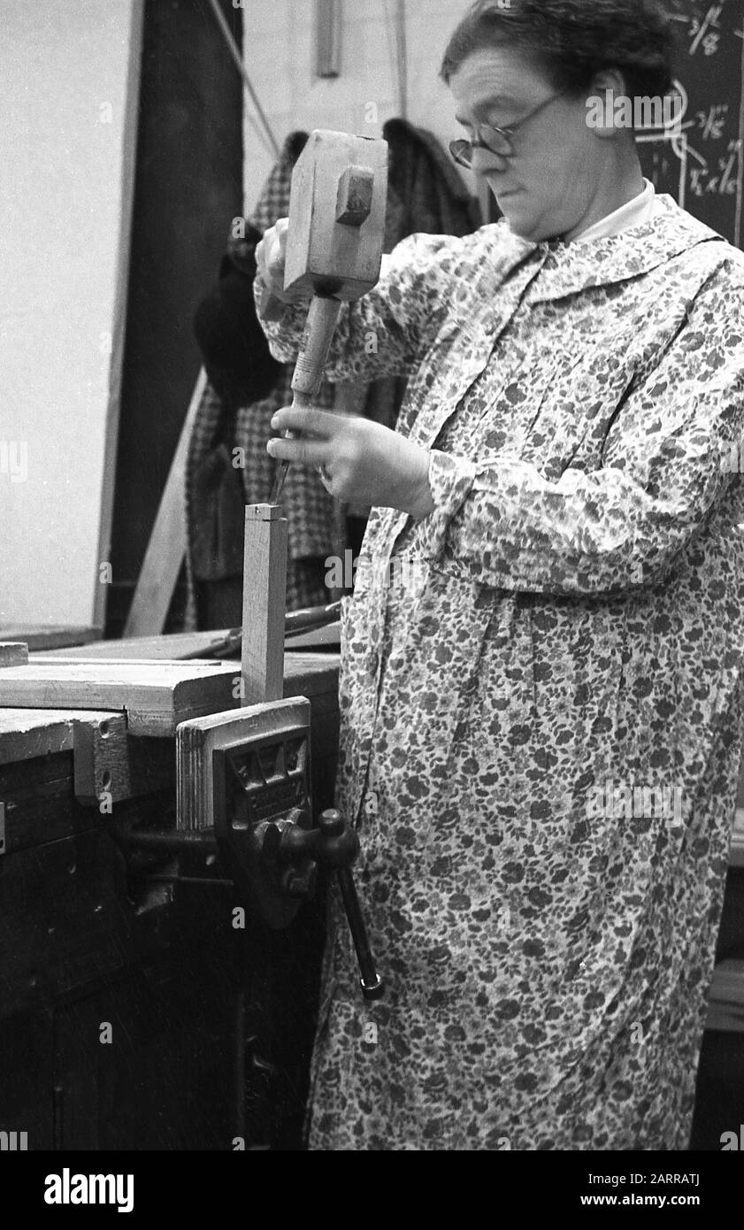 1948, historical, a lady wearing a long sleeve flower patterned overgarment or pinafore, standing at a workbench, using a wooden hammer and chisel during an evening adult woodworking class, London, England, UK. Stock Photo