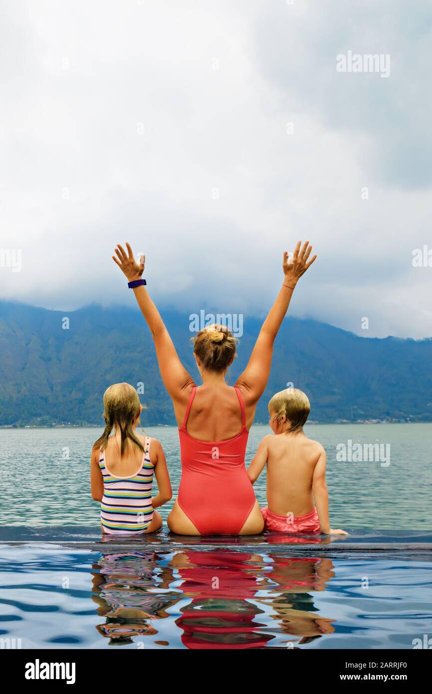 Happy family in Batur volcano hot spring spa. Travel in Kintamani, Bali. Mother, kids chilling in infinity pool with lake view. Healthy lifestyle Stock Photo
