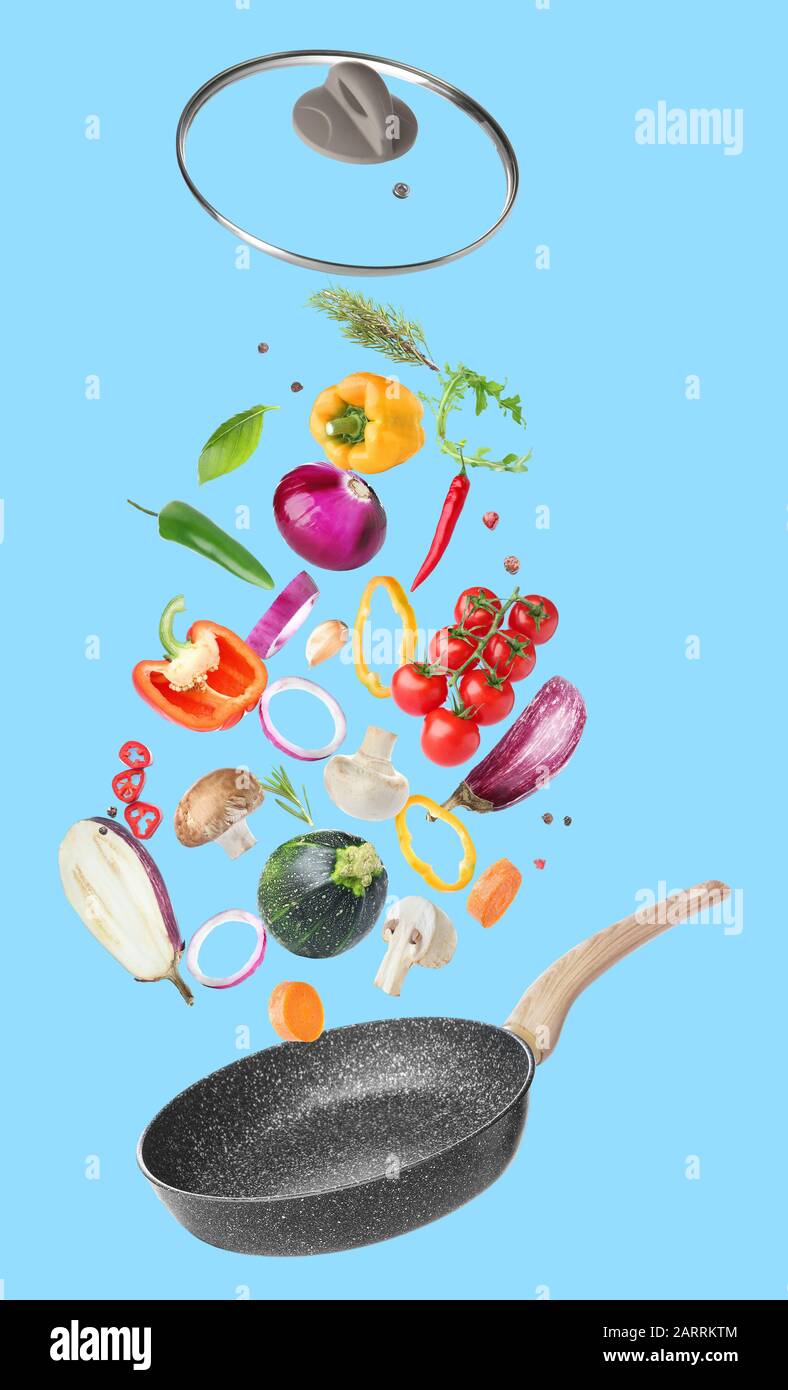 Frying pan and flying vegetables on color background Stock Photo