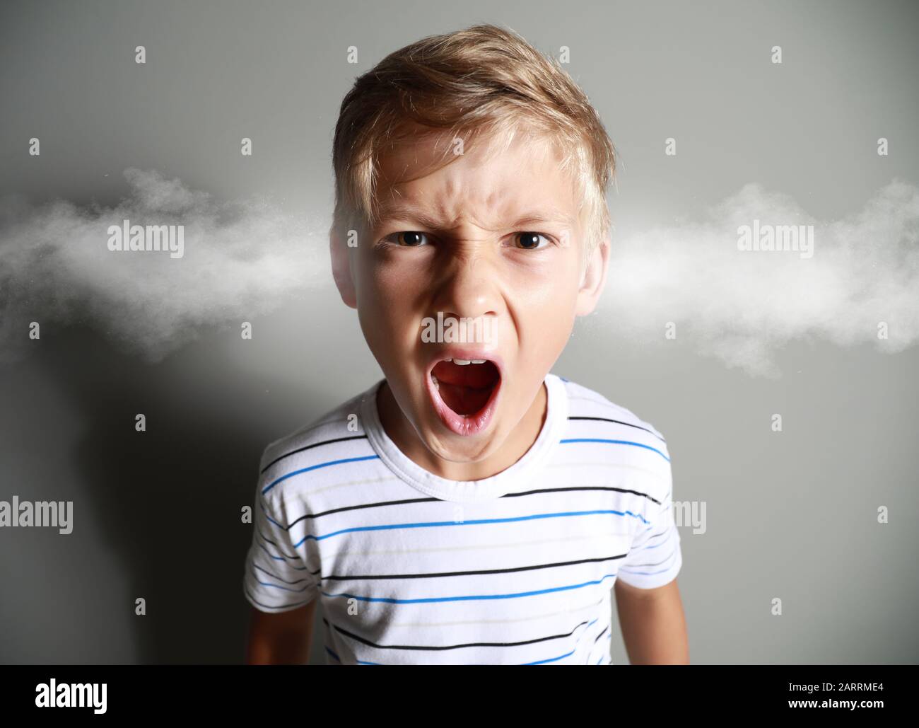 Portrait of angry little boy with steam coming out of ears on grey background Stock Photo