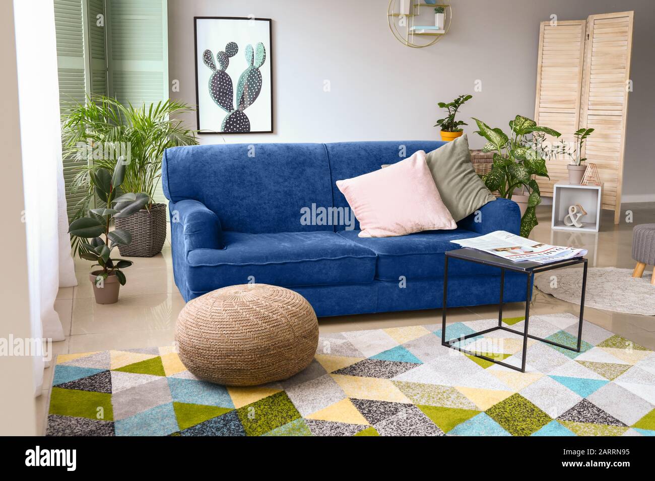 Stylish interior of room with blue sofa and green houseplants Stock