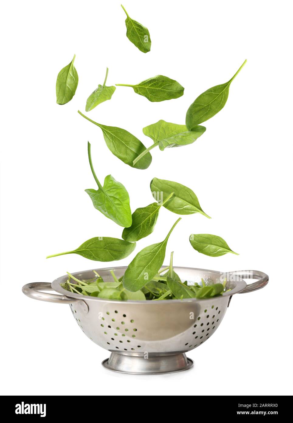 Colander with falling spinach on white background Stock Photo