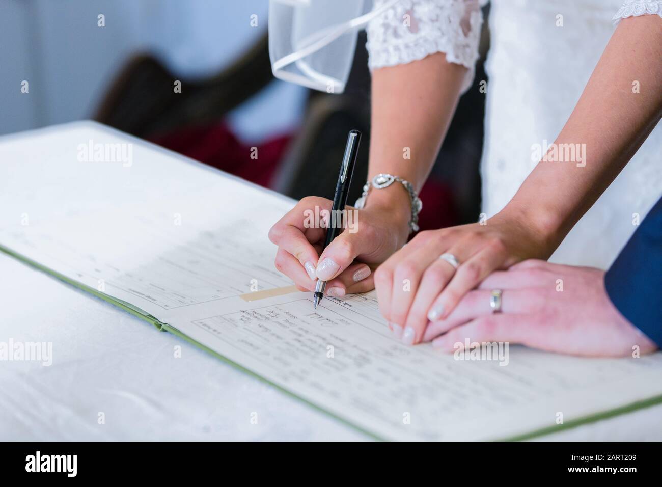 A bride and groom sign a church marriage registration book following their church wedding. Both wedding rings are clearly visible Stock Photo