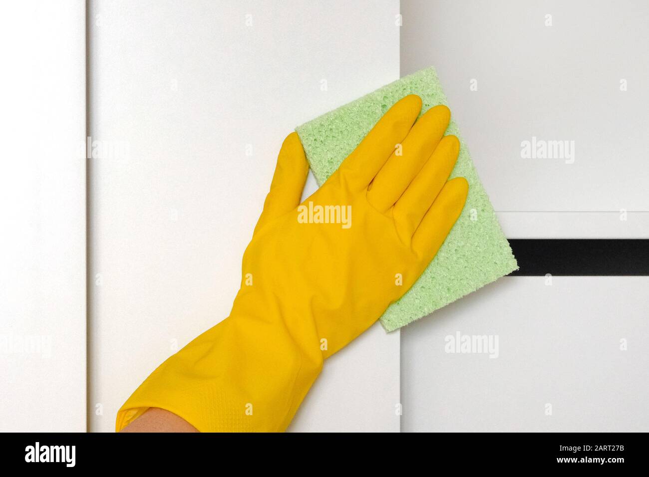 Hand in rubber protective glove with microfiber rag is cleaning cupboard in room. Wiping white shelf from dust. Сleaning or regular clean up. Stock Photo