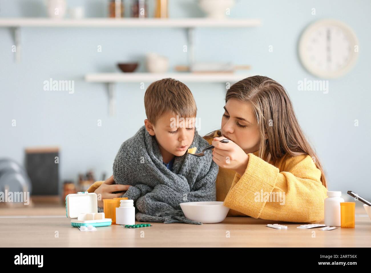 Mother feeding her sick son with chicken soup in kitchen Stock Photo
